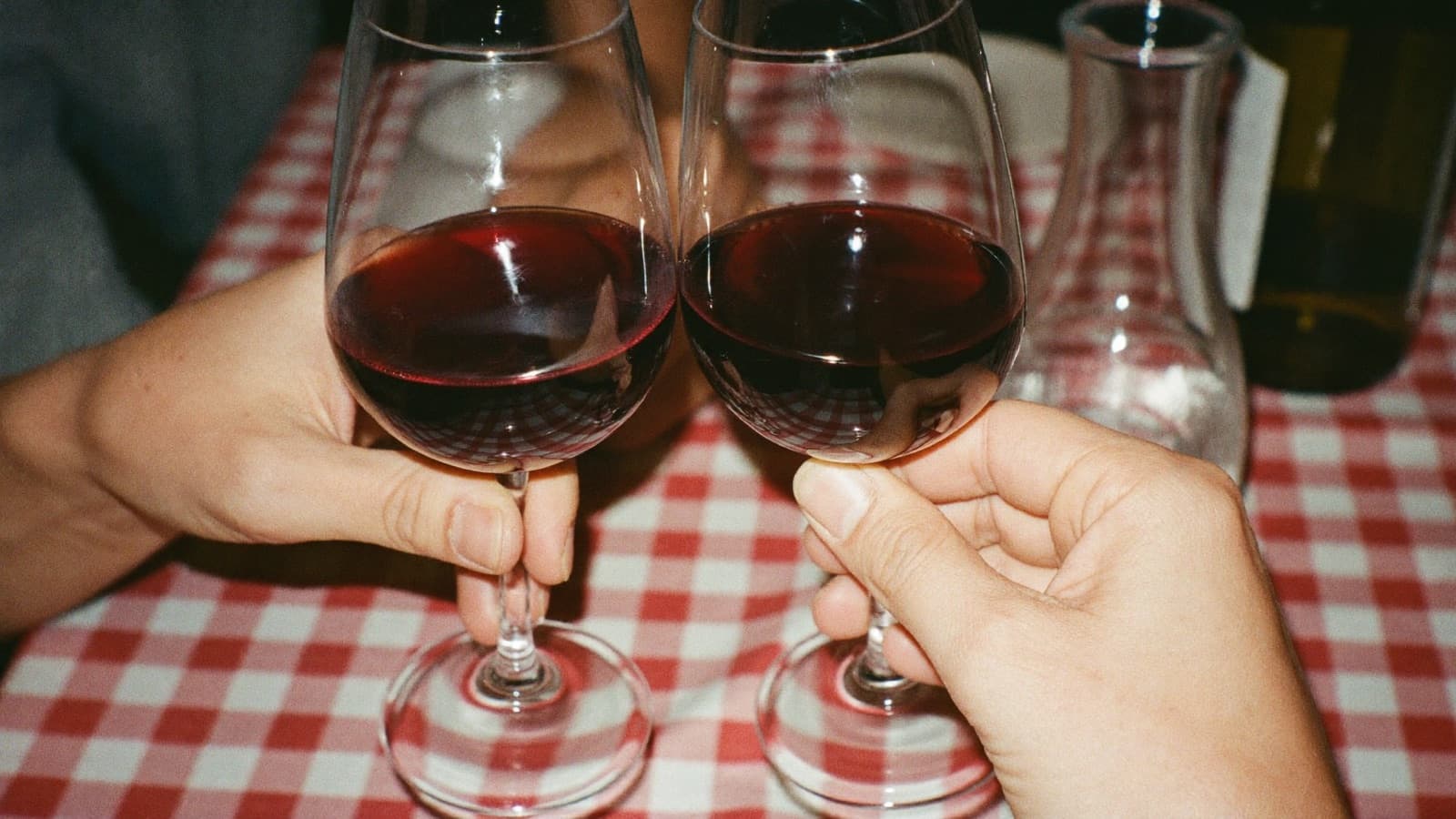 Two friends clinking modest glasses of red wine over a casual bistro table