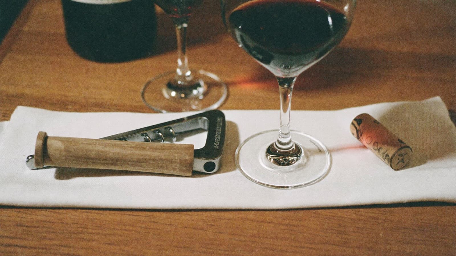 A guest handing a wine bottle across the table to a server holding a corkscrew