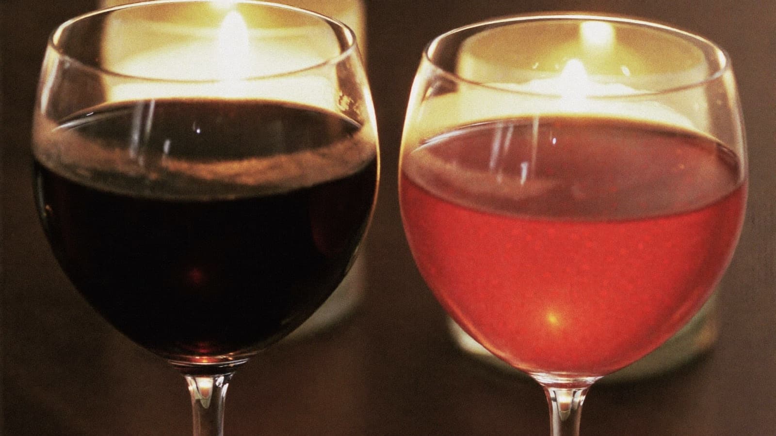 Two glasses of red wine side by side, one deep and dark, one pale ruby, in candlelight