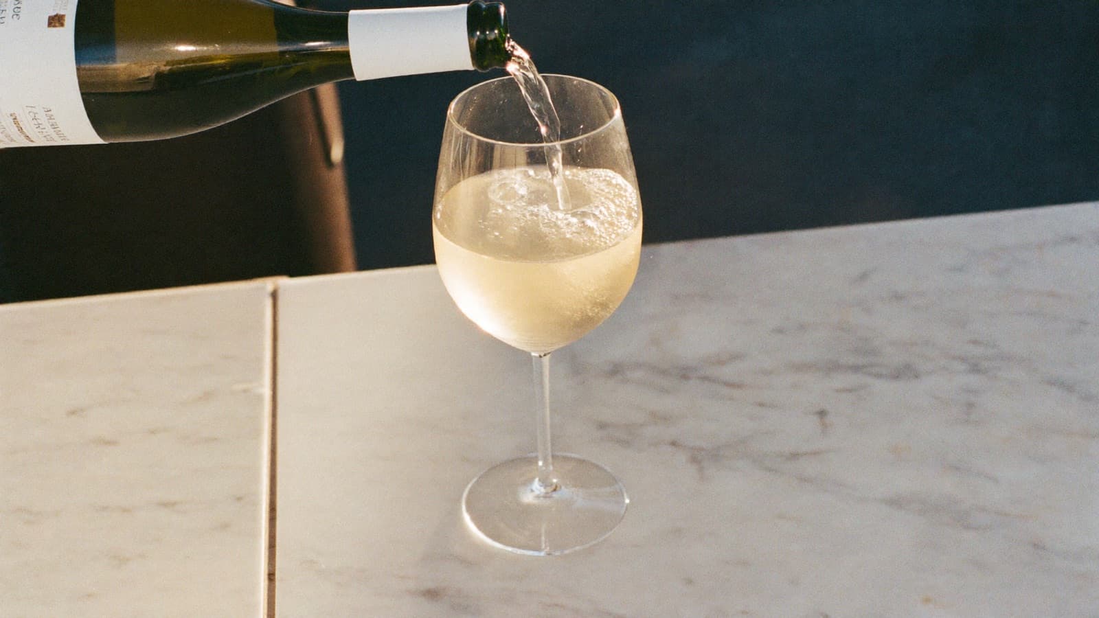 A modest pour of white wine in a large glass on a bright marble bar top