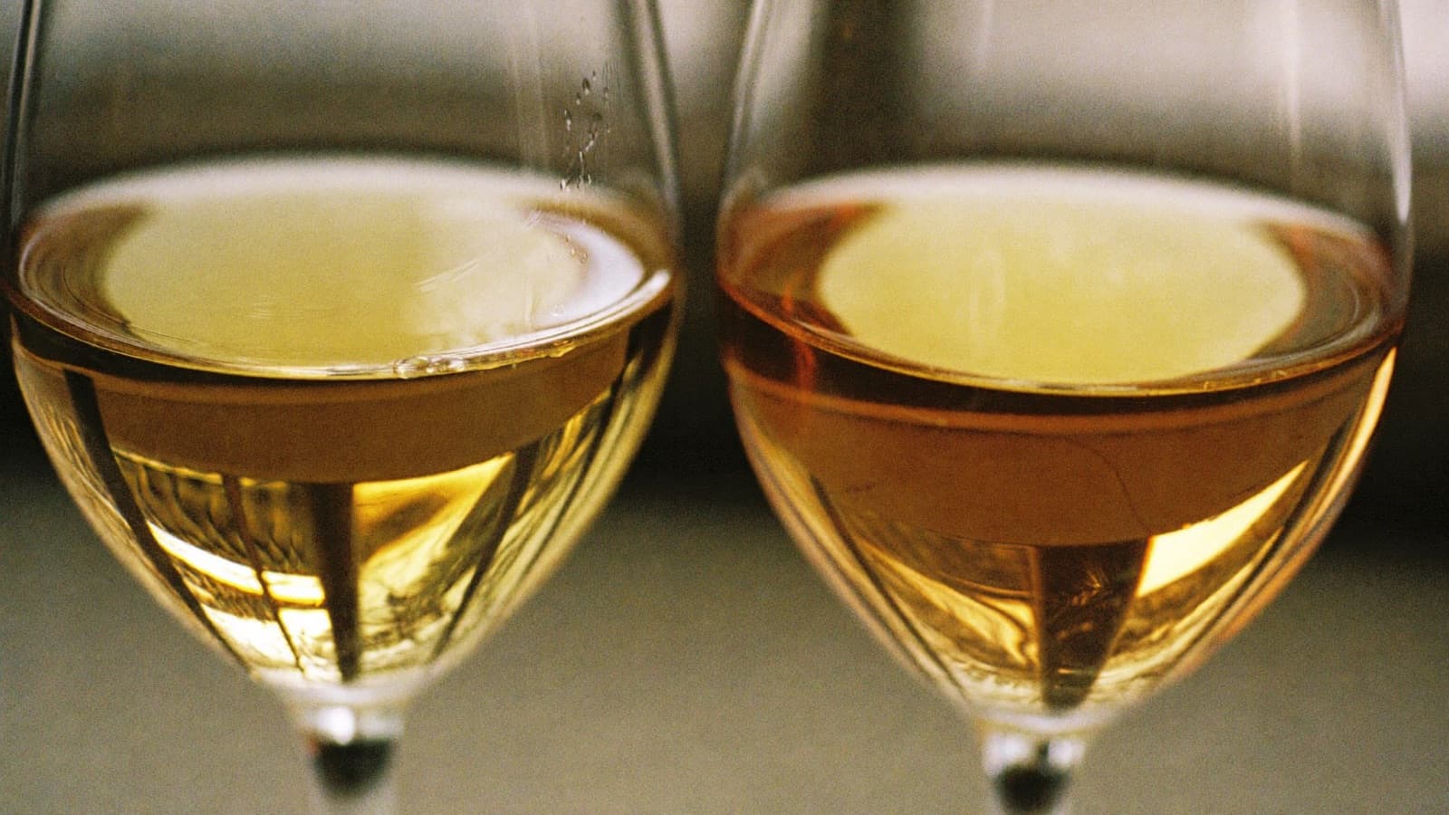 Two glasses of white wine side by side, one golden, one pale straw, in window light