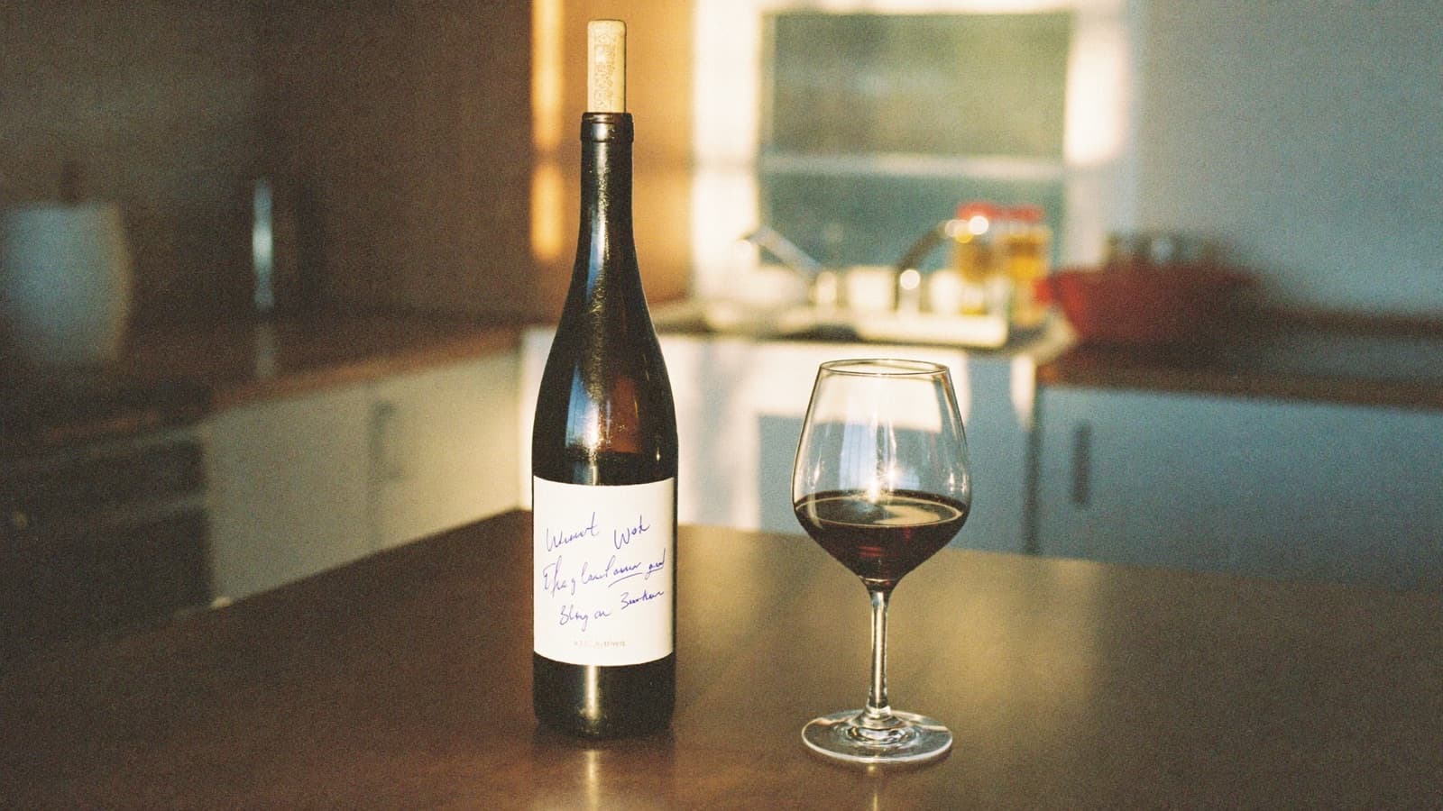 A re-corked wine bottle on a kitchen counter at golden hour beside a half-full glass