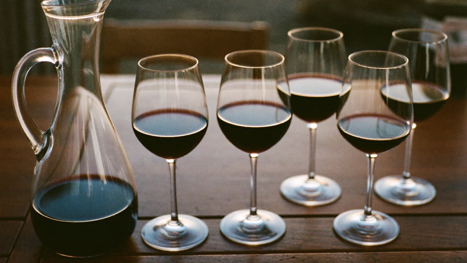 A wine bottle standing beside five equal pours of red wine in a row