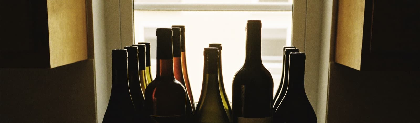 A dozen wine bottles resting on a small countertop rack in a warm apartment kitchen