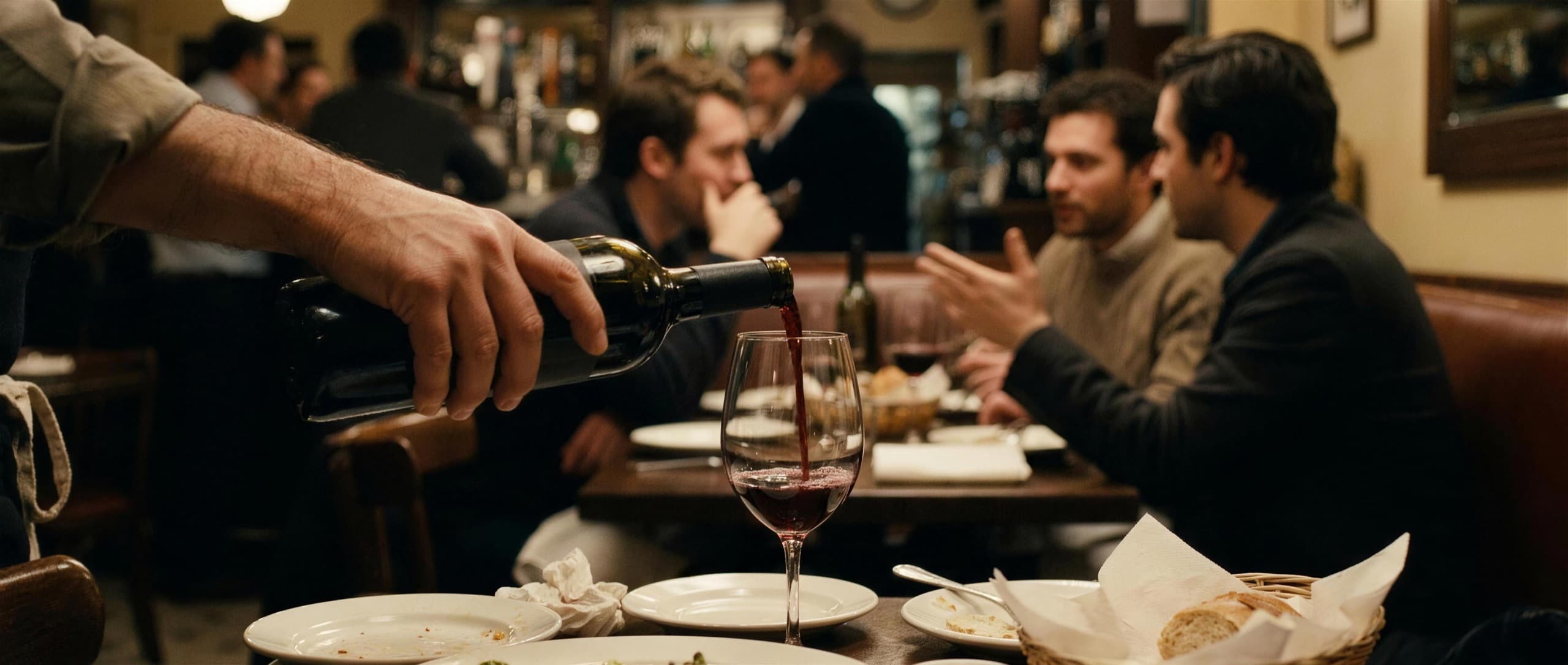 A server pouring a glass of red wine at a busy neighborhood bistro