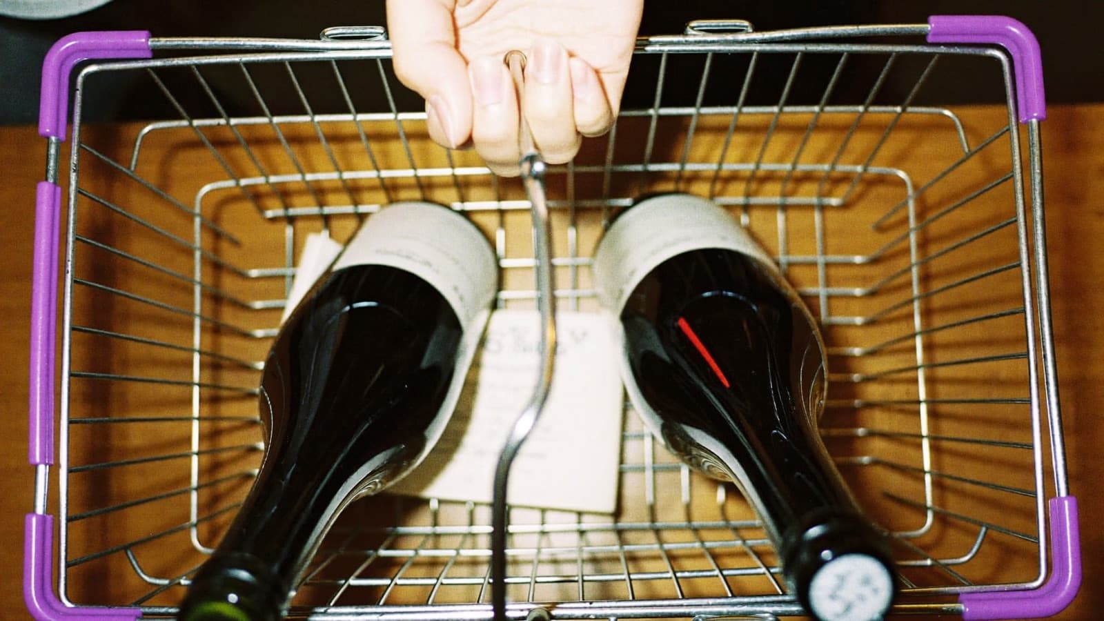 A hand lifting a wine bottle from a bright grocery store shelf