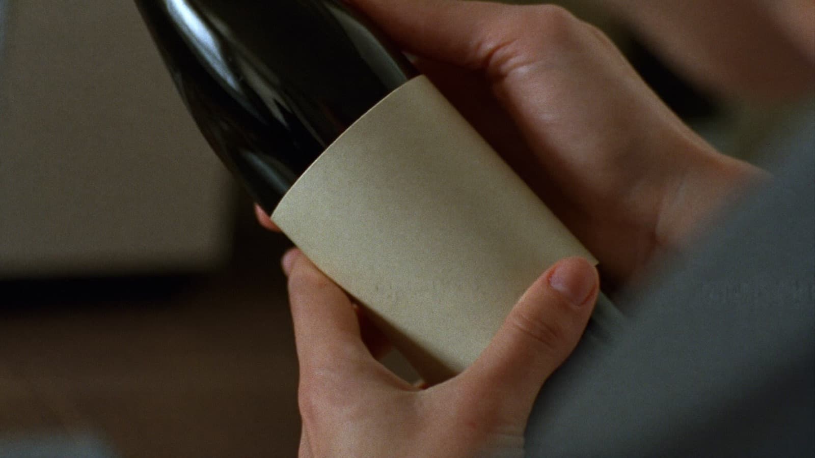 Hands turning a dark wine bottle to examine it at a kitchen table