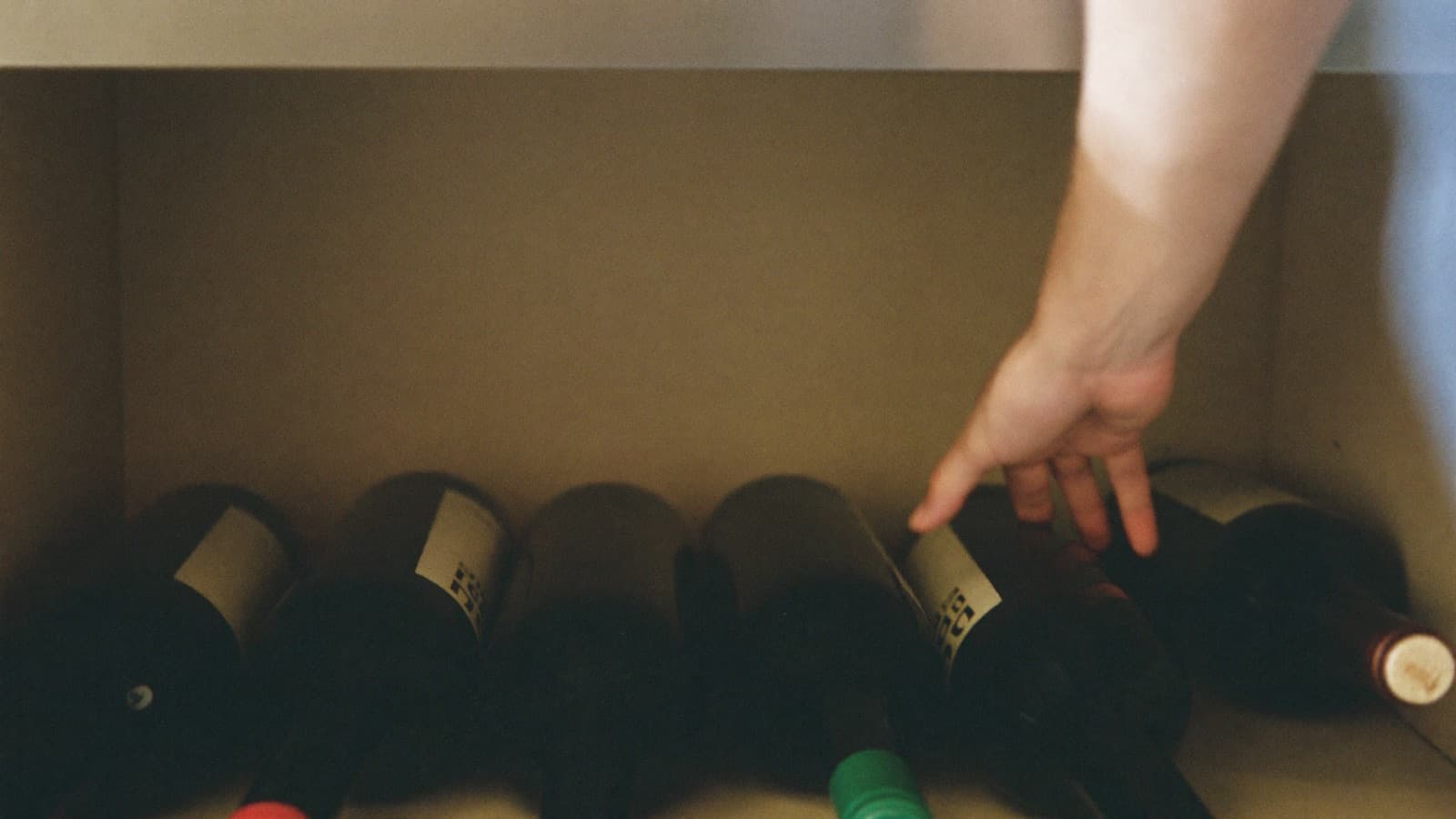 A hand sliding a wine bottle onto its side in a cool kitchen cabinet