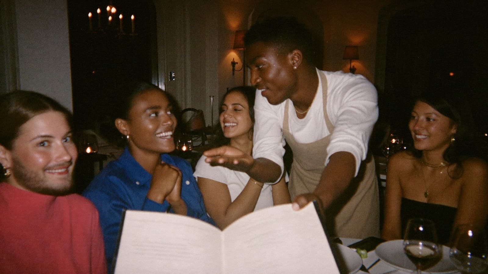 A friendly sommelier leaning in to chat with seated dinner guests