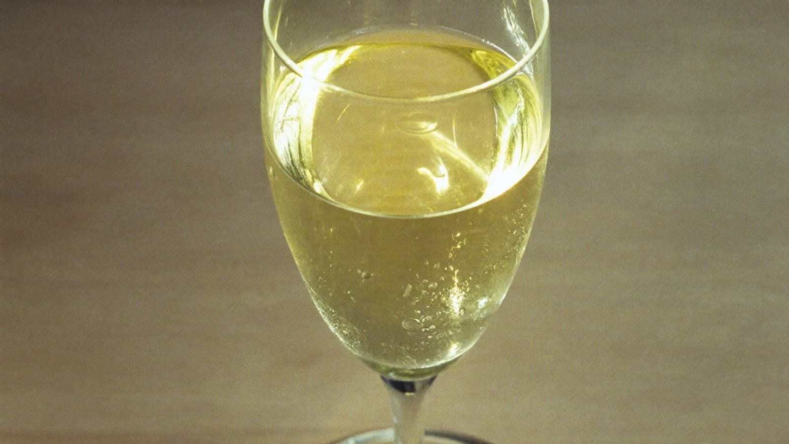 A tall slender glass of pale golden white wine with condensation in bright airy light