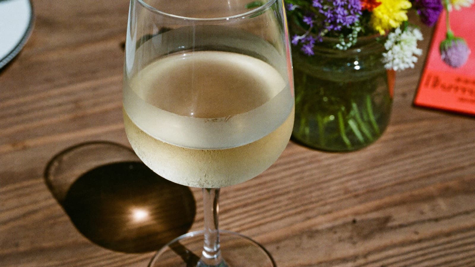 A tumbler of cloudy natural wine on a rustic table beside wildflowers