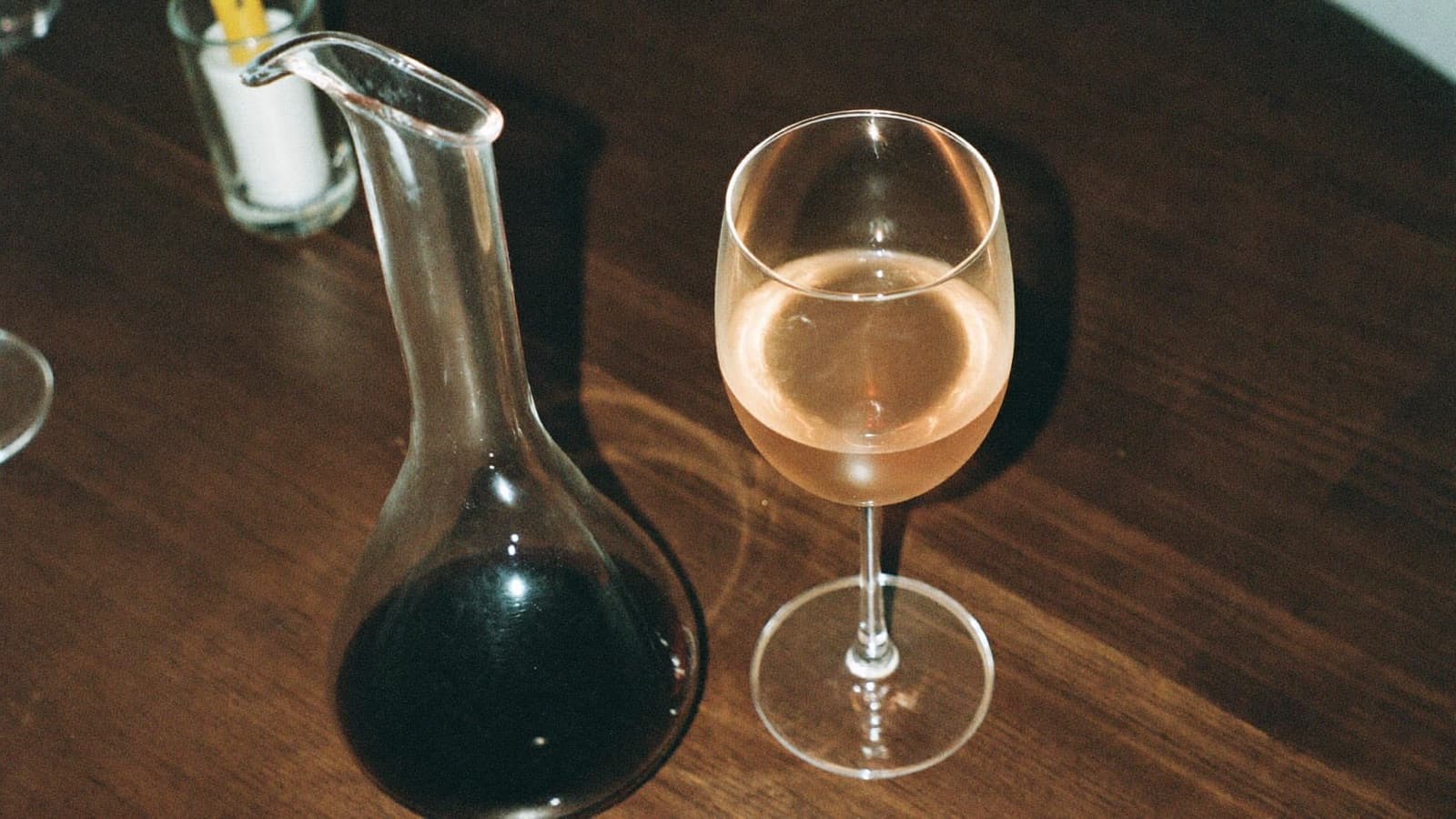 Pale garnet red wine in a wide glass beside a decanter by candlelight