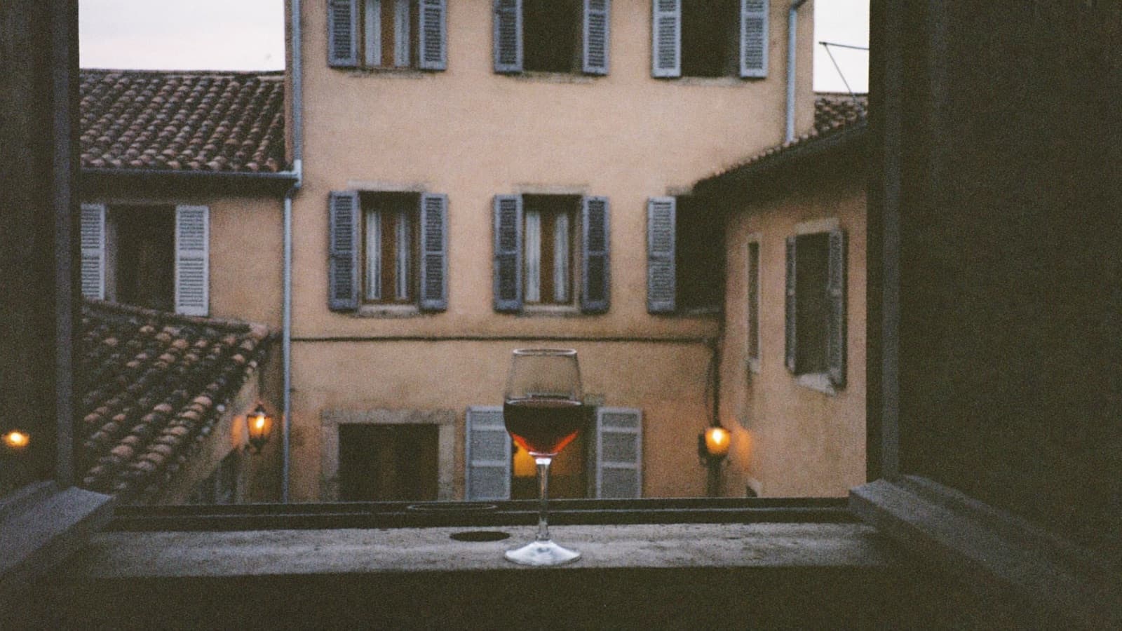 A glass of red wine on a weathered stone windowsill in an old European courtyard at dusk