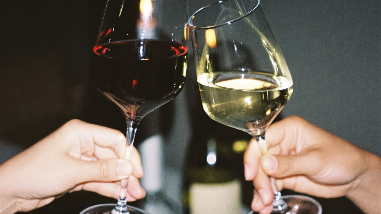 A glass of red wine and a glass of white wine touching mid-clink