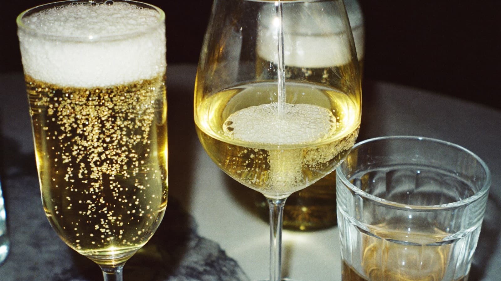 Three sparkling wines fizzing in a flute, a tulip glass and a tumbler on a marble bar