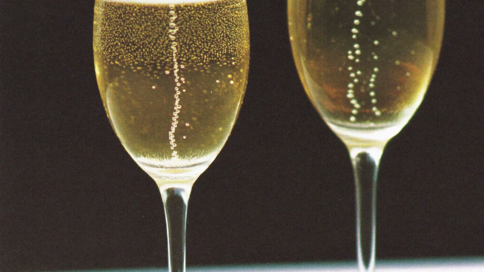 Two flutes of sparkling wine with fine bubble streams backlit in gold