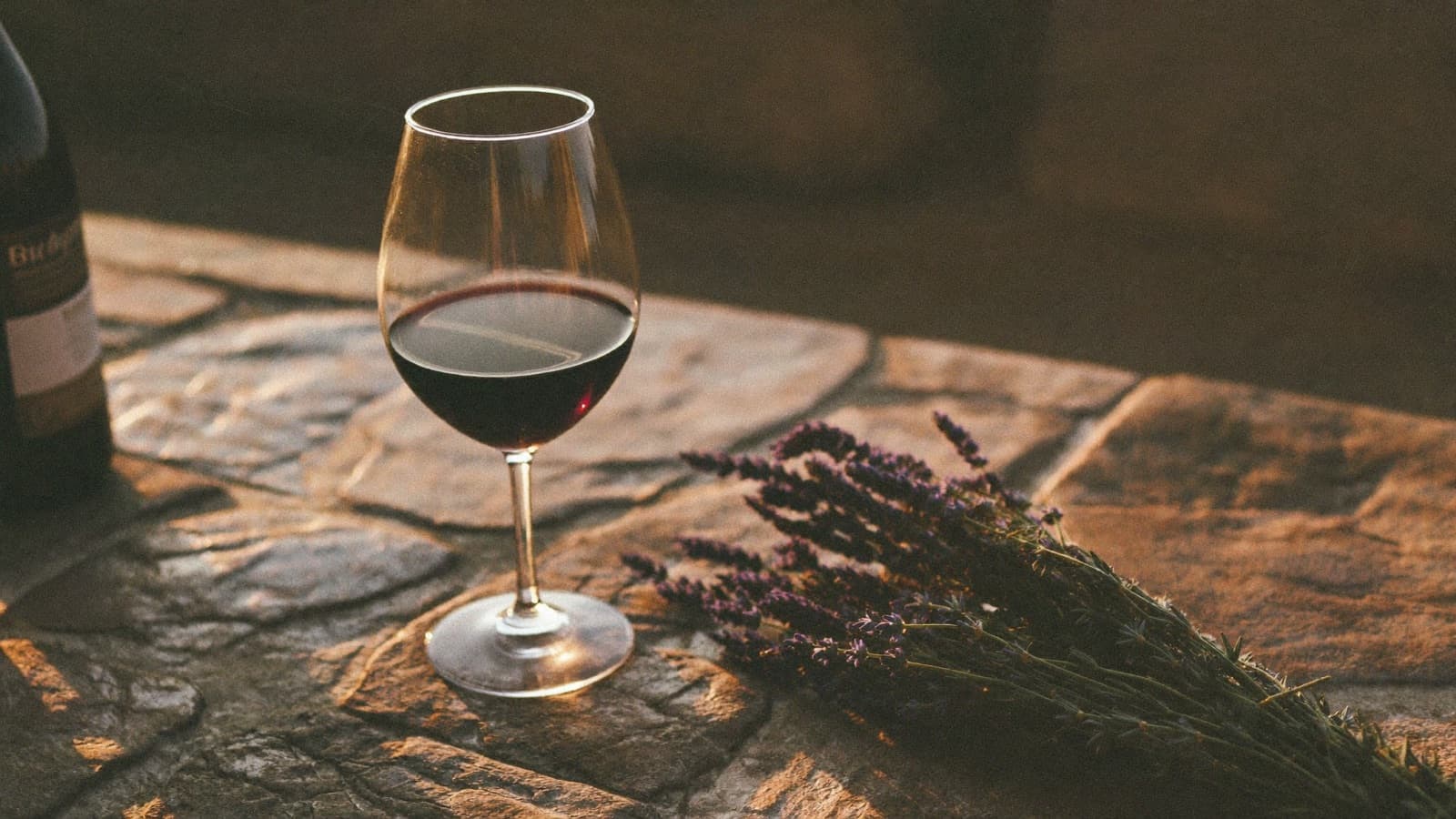 A glass of deep garnet red wine on a rustic stone table with dried lavender