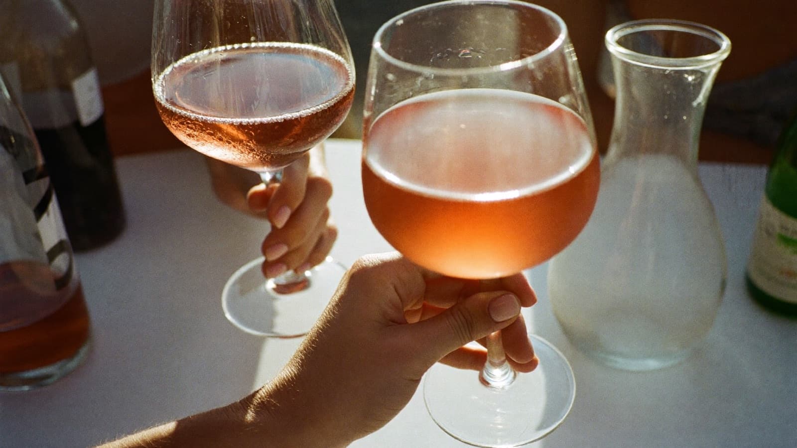 Two glasses of pink rosé and a small carafe on a sunlit patio table