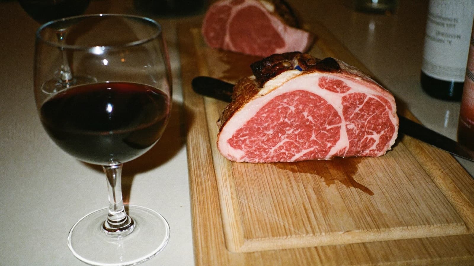 A glass of deep red wine beside a sliced ribeye on a wooden board