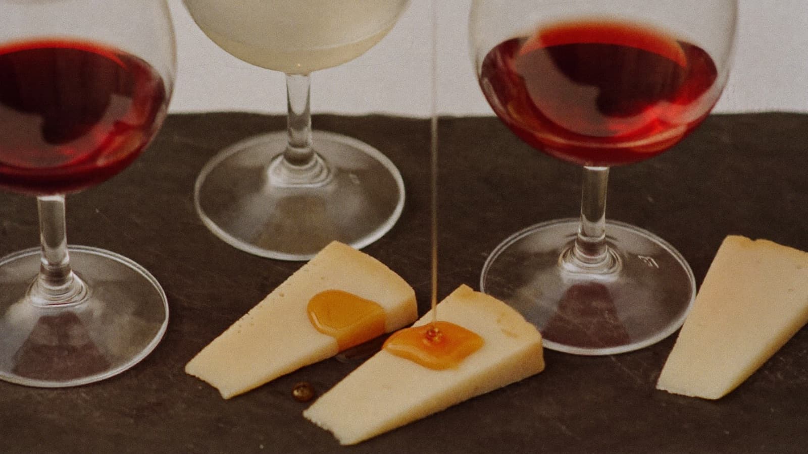 Glasses of red and white wine beside a trio of cheese wedges on a slate board