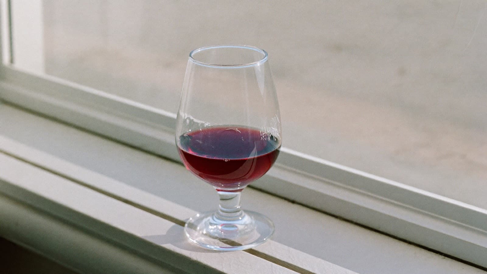 A half-finished glass of red wine on a bright windowsill in morning light