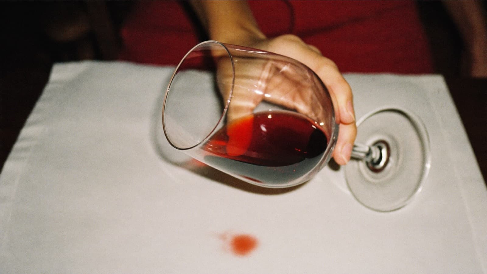 A hand tilting a glass of red wine over a white napkin to inspect its color
